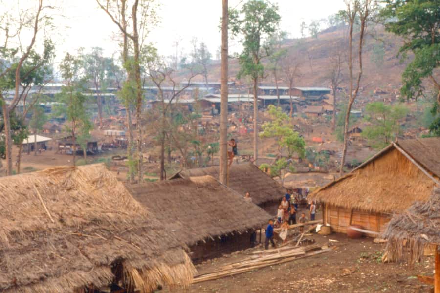 Thatched houses on a cleared hillside at Ban Vinai, with forest behind
